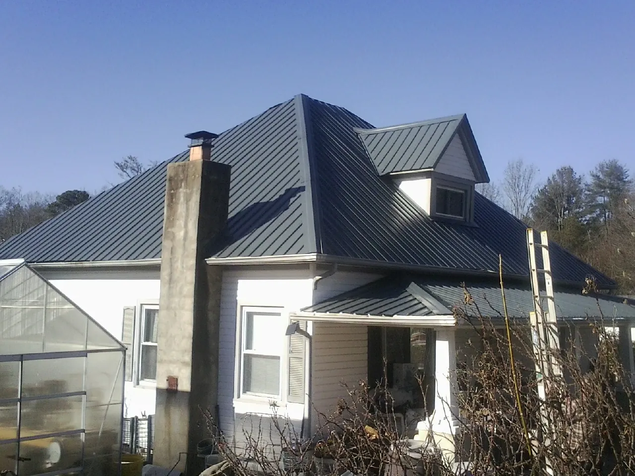 Dark blue standing seam metal roof on a white farmhouse with dormer — Slate & Tile Roof Repair by Roofing Brothers in Bunnell