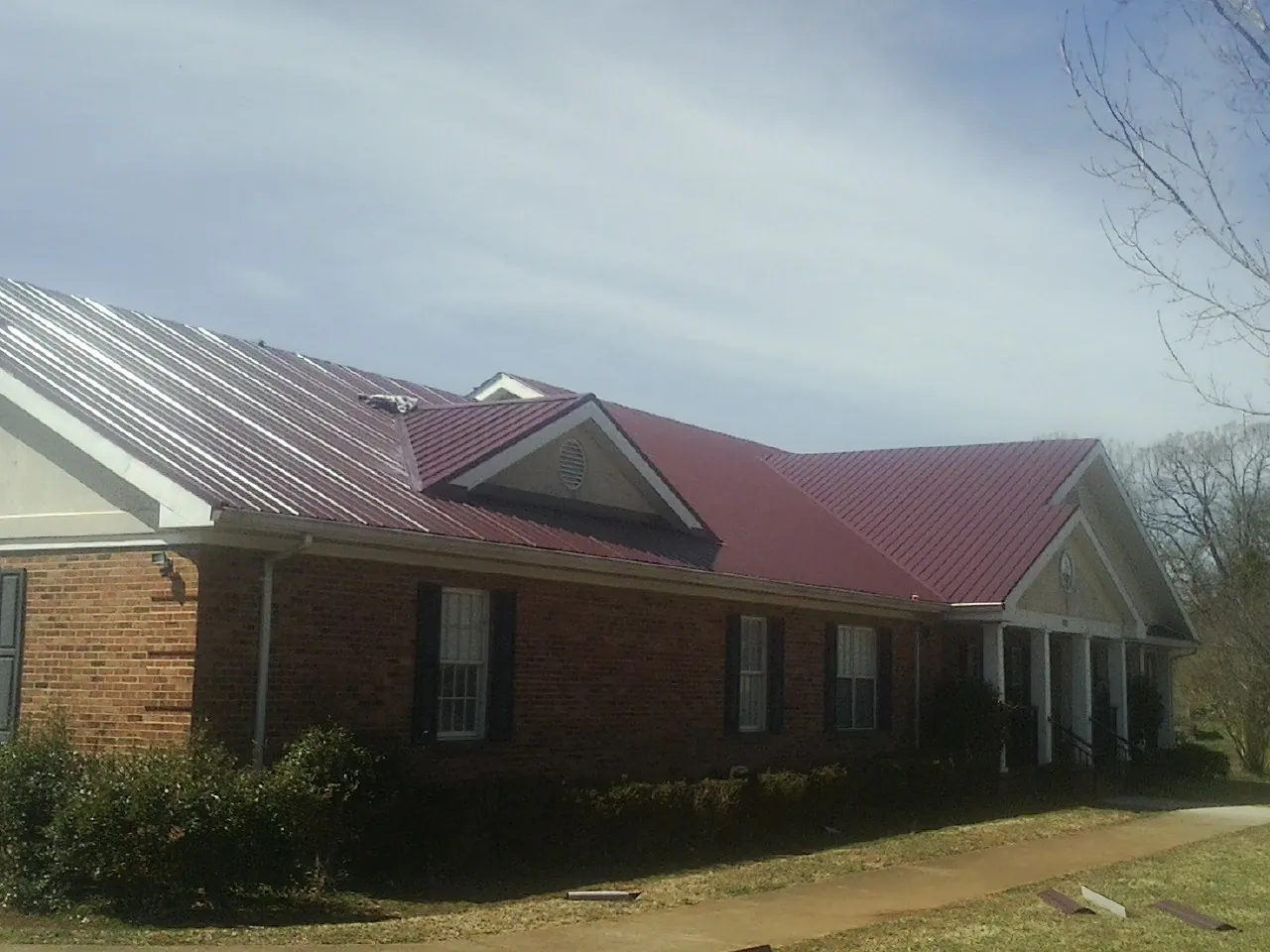 Red metal roof with gabled entries on a long brick building, from a Hail Damage Roof Repair job in Bunnell