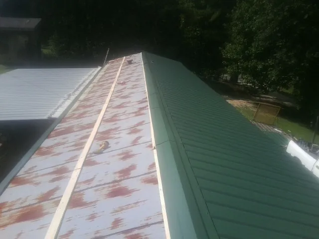 Old rusted panels beside newly installed green metal roofing — Wind Damage Roof Repair by Roofing Brothers in Bunnell
