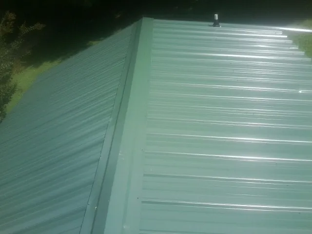 New green metal panels meeting at the ridge of a roof — Flat Roof Repair work by our crew in Bunnell