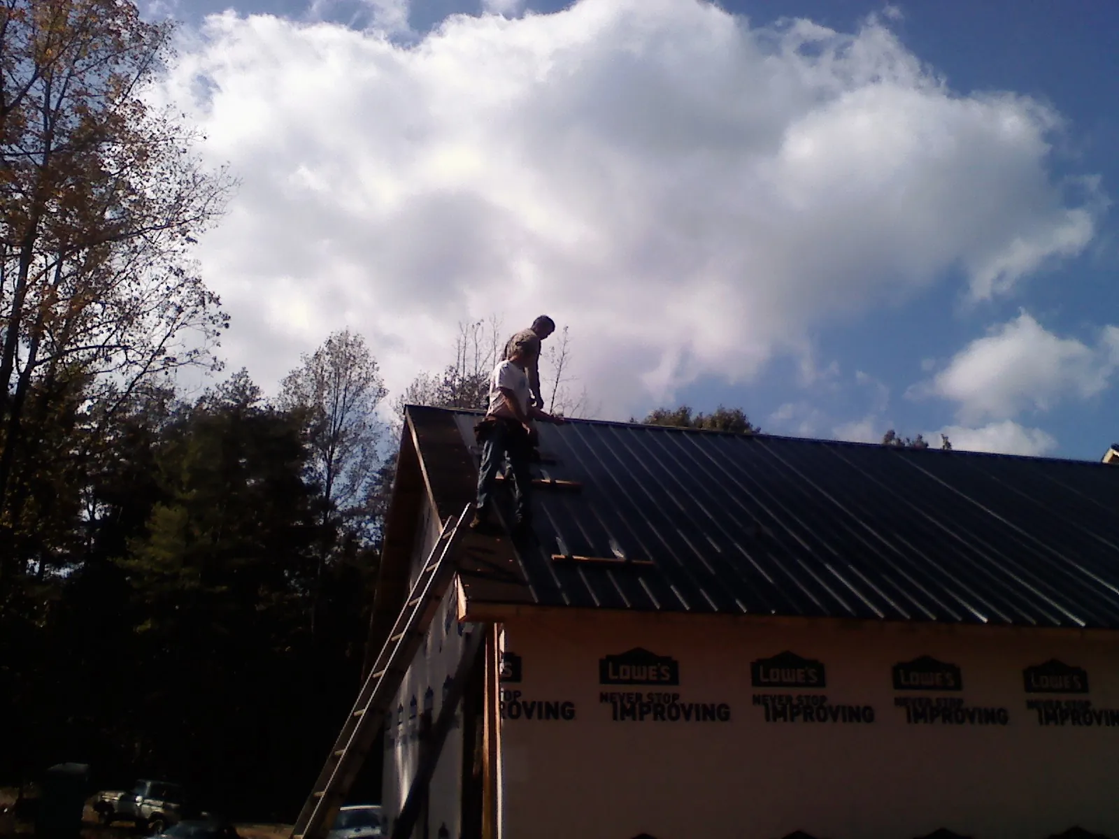 Roofer fastening dark metal panels high against a cloudy sky, from a Roof Inspection job in Bunnell