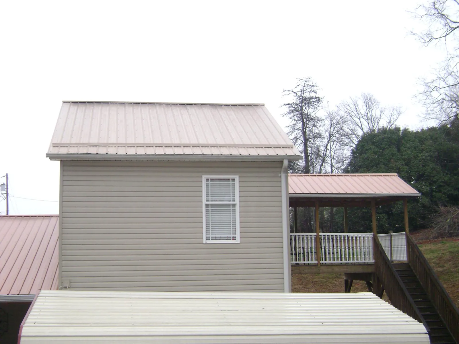 Tan metal roofs on a two story addition and attached porch, from a Roof Replacement job in Bunnell